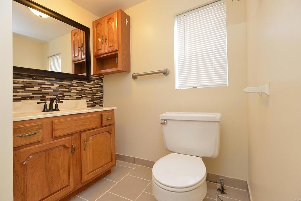 Finished bathroom with wood vanity, mosaic backsplash, tile floor, and white fixtures